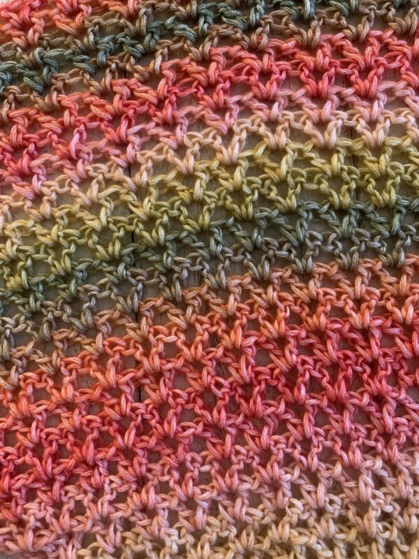 crochet shawl in the color strawberry patch on a white board background